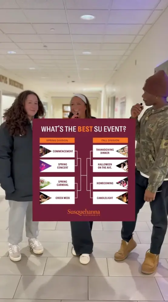 Three students stand in a hallway while one holds a microphone. In front of them is a bracket chart titled "What's the BEST SU Event?" with various Susquehanna University events listed for Spring and Fall divisions.